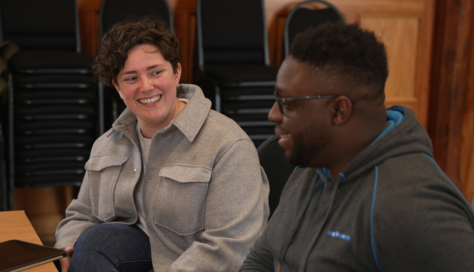 A black man chatting to a white women, who has a notepad, in the wooden-panelled Parry rooms.